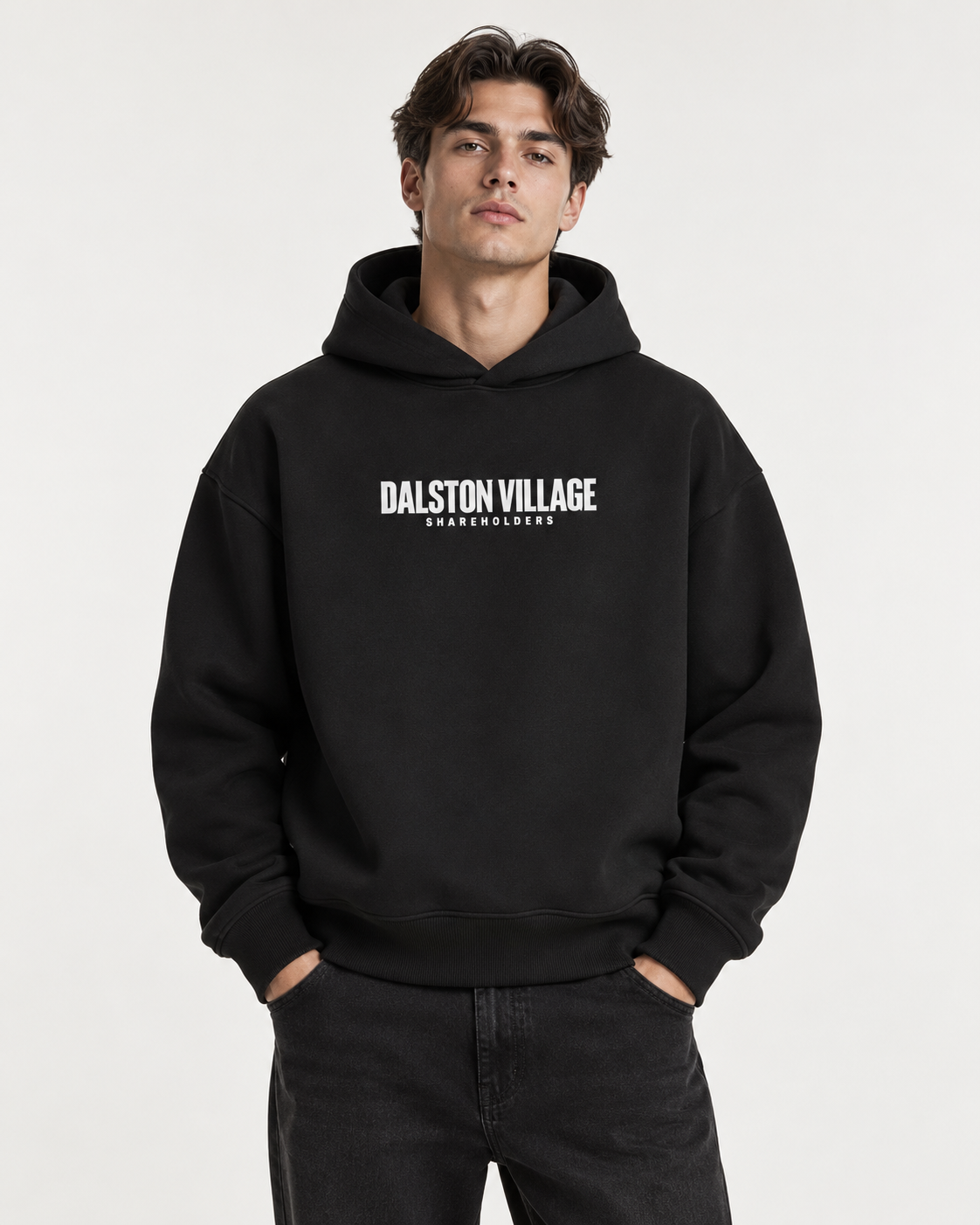AI-generated studio styling visual of a male model wearing the black Dalston Village Shareholders heavyweight hoodie with white chest branding. Not a physical fit photograph.