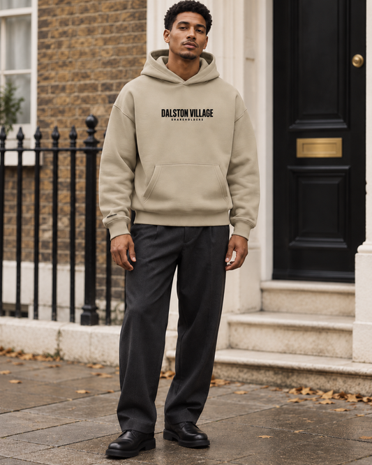 AI-generated editorial mockup of a model wearing the sand Dalston Village Shareholders hoodie with charcoal trousers.
